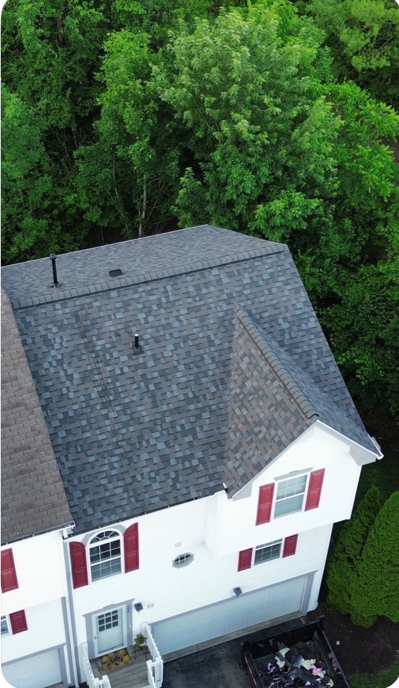 Aerial view of a new gray shingle roof on a wooded two-story home