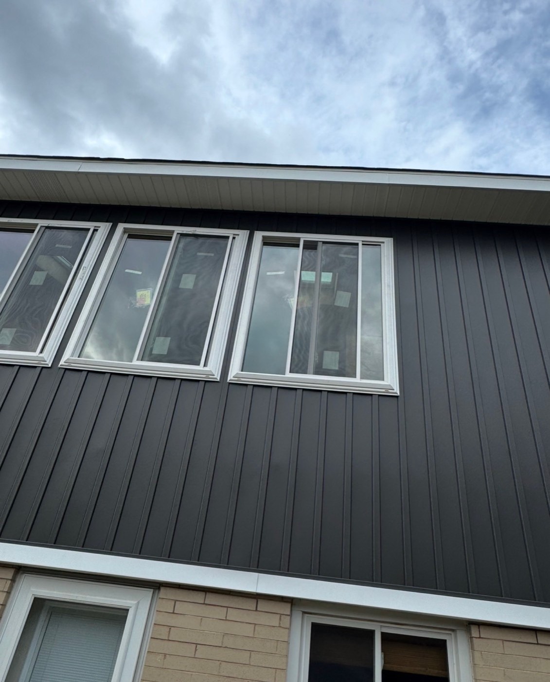 Close-up of new dark board-and-batten siding and white trim windows