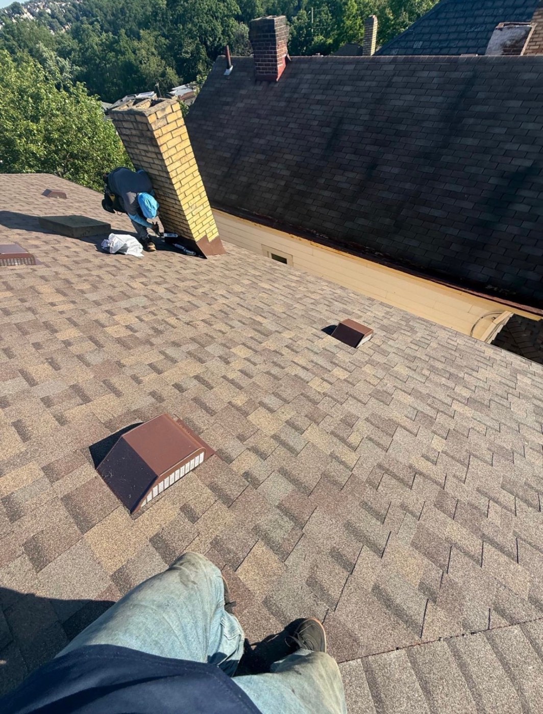 Crew finishing a brown blend shingle roof beside a brick chimney